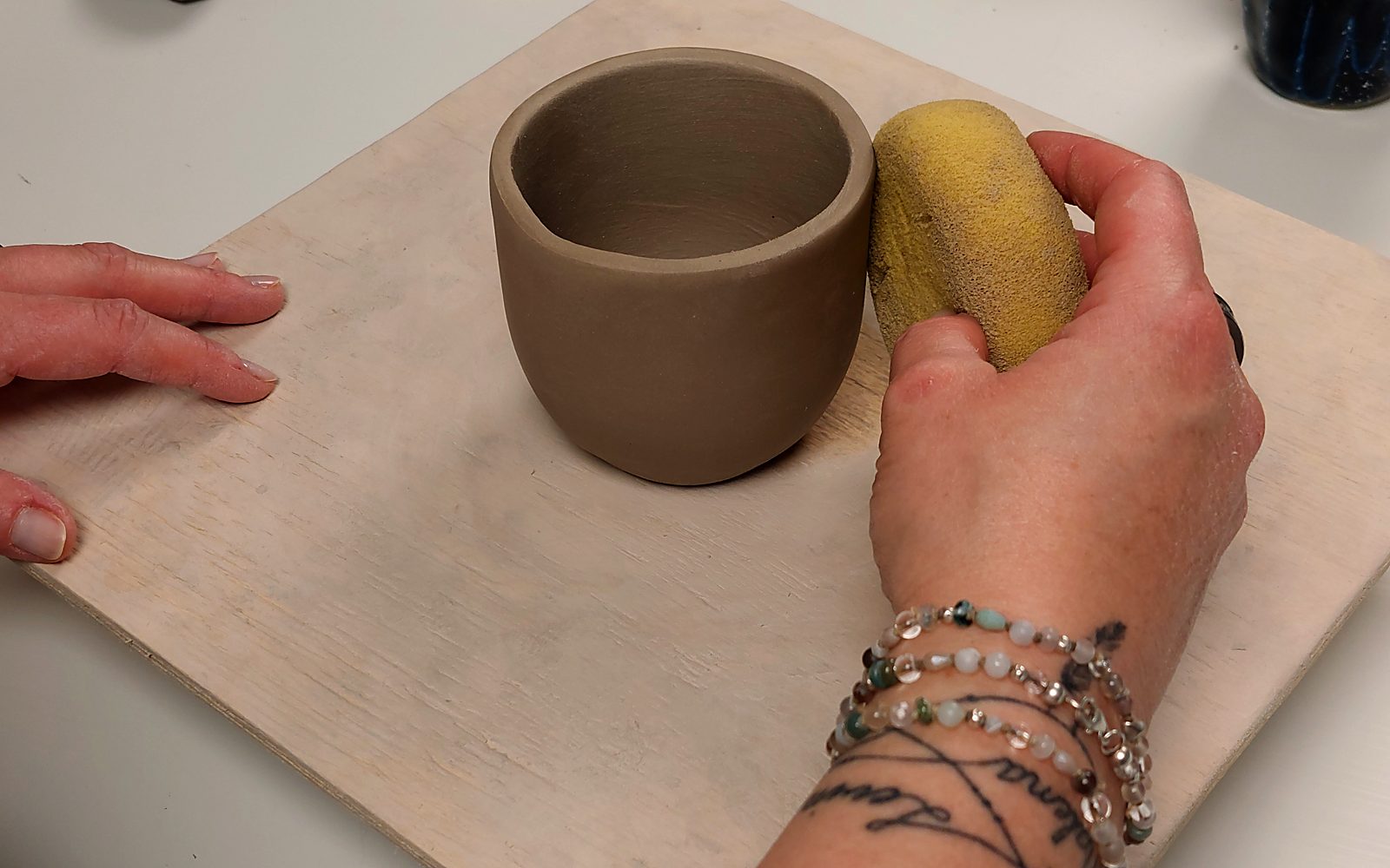 Hände glätten einen frisch aufgebauten Becher aus Ton